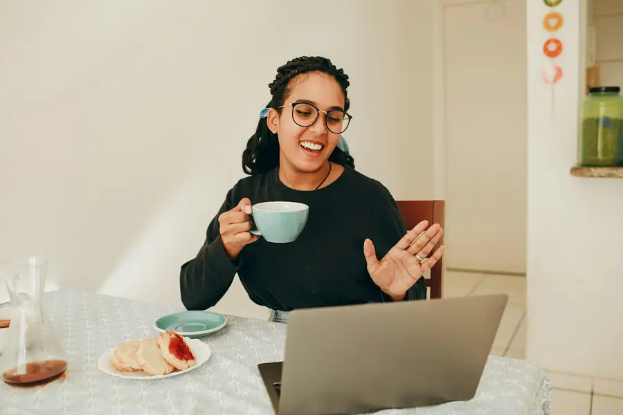 A woman on a video call at home, a cup of tea beside her laptop.