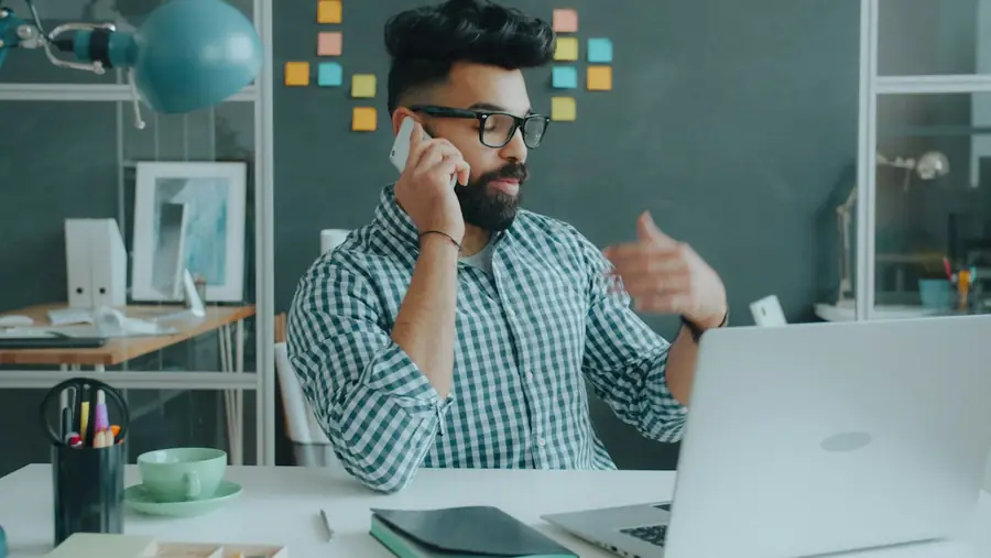 A man on a call at his desk, talking a plan through.