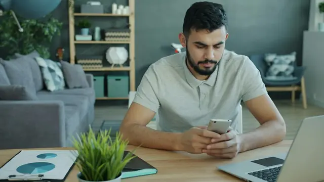 A man at his desk scrolling through his phone.