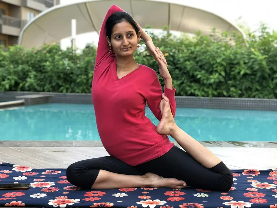 A woman holding a yoga pose on a mat beside a rooftop pool.