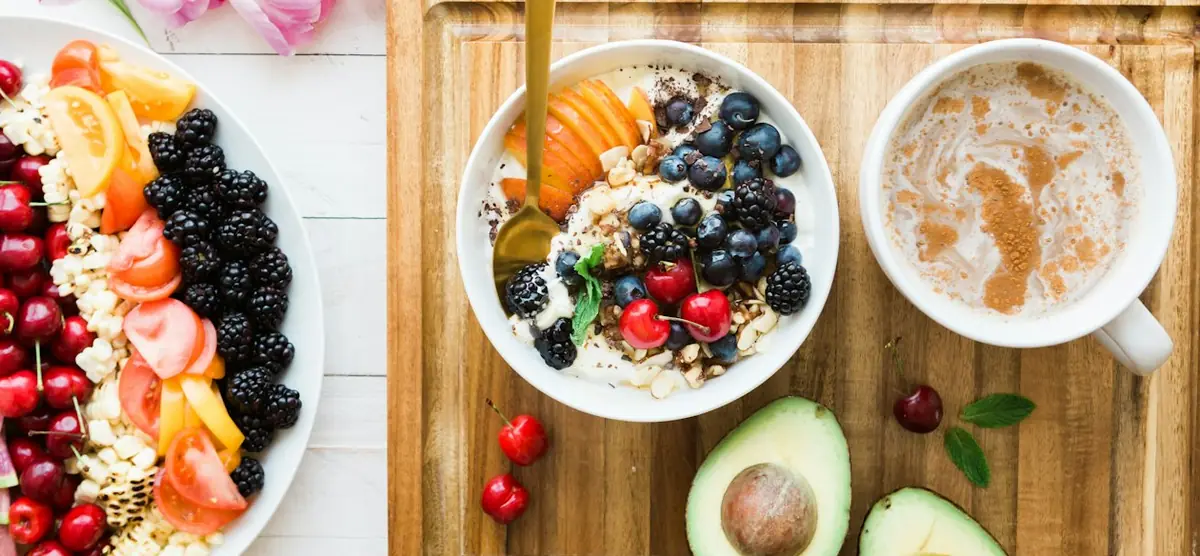 A fresh breakfast spread: a yoghurt bowl with berries, a platter of fruit and a coffee.